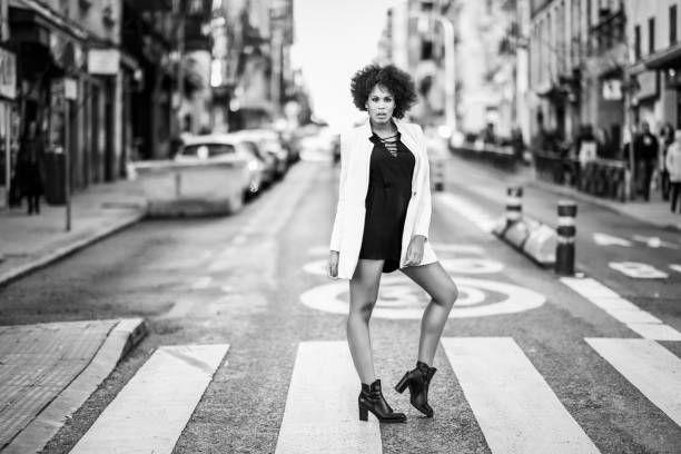 Woman in a stylish black and white outfit confidently poses on a city street crosswalk.