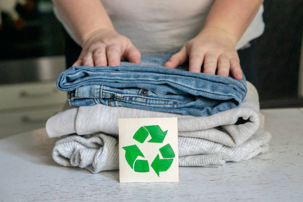 Hands organizing folded clothes with a recycling symbol, representing sustainable fashion choices.